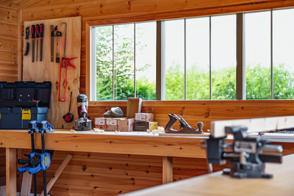 Window Security for Superior Sheds Timber garden workshop with window security bars, a long workbench, bench vice, hand plane, toolboxes and neatly organised tools.